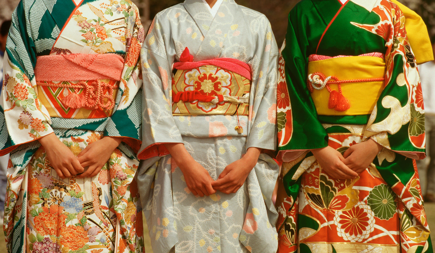 Three women wearing colourful traditional kimonos with decorative obi belts, standing side by side.