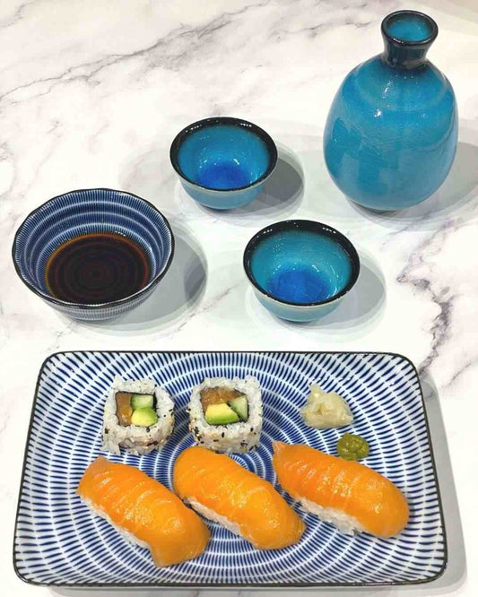Blue and white Japanese sushi plate with nigiri, maki, ginger and wasabi on. Behind this, a small bowl holds soy sauce.
