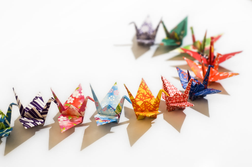 A line of authentic Japanese origami cranes made from patterned paper on a white backdrop