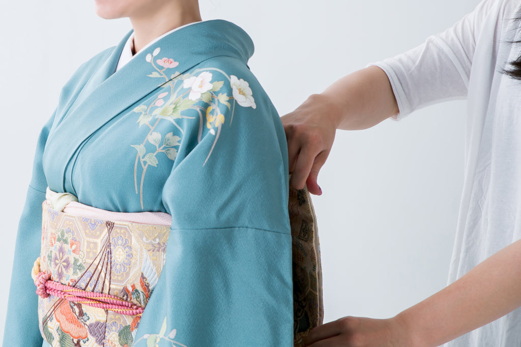 Someone adjusting the obi on another's floral, blue kimono