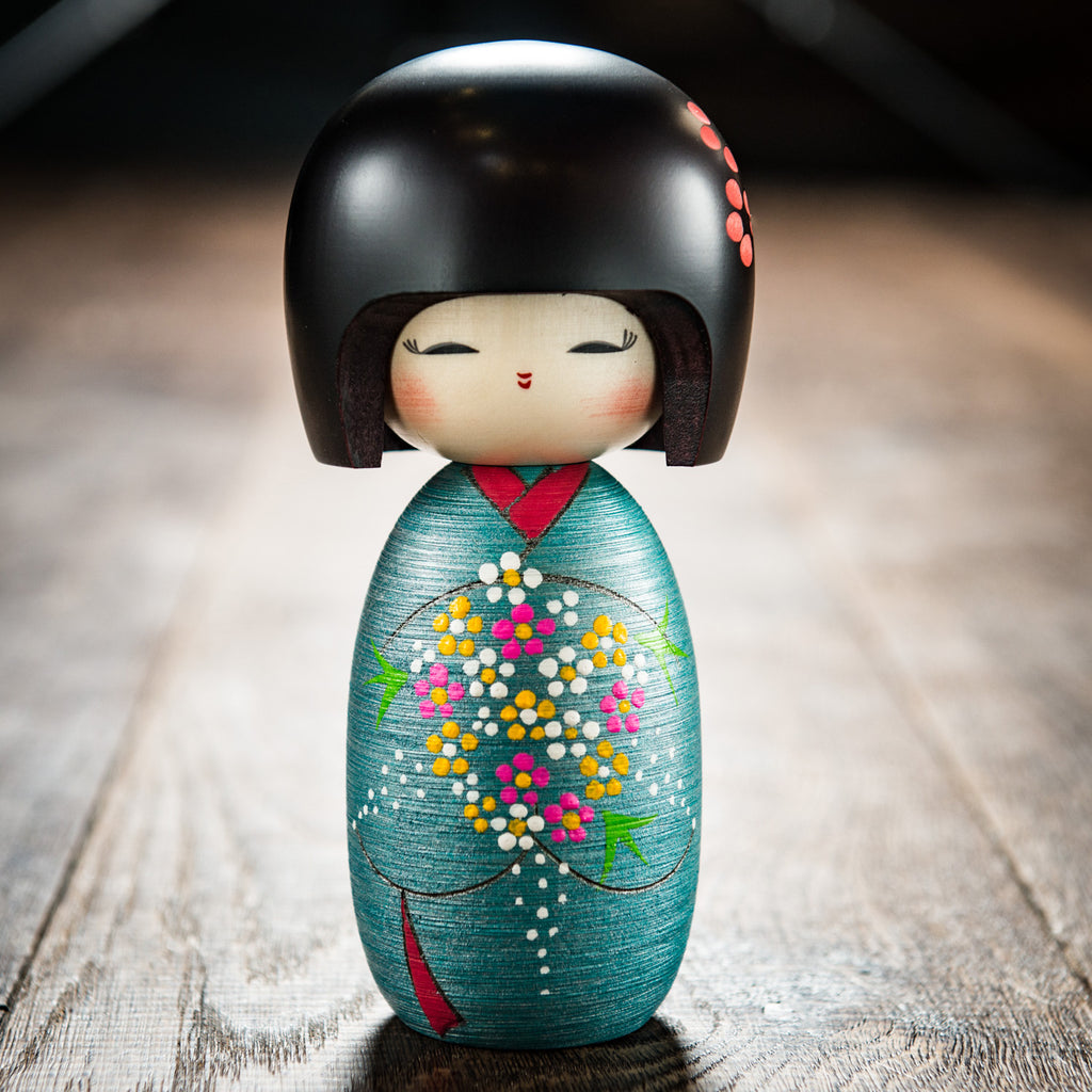 Japanese traditional kokeshi doll with sleek black bob, serene visage and floral green kimono