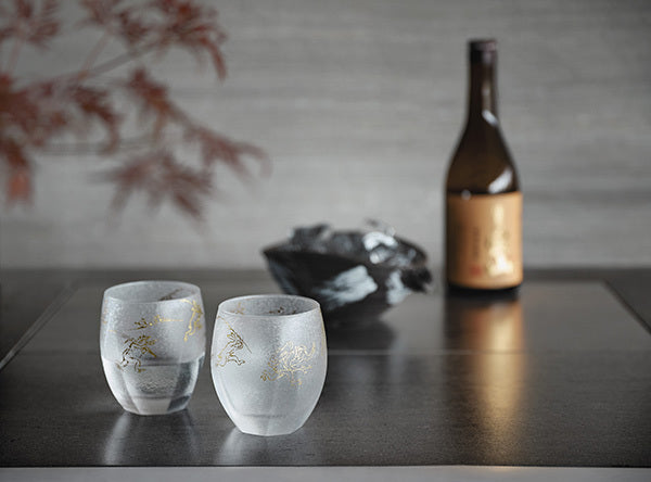 Two gold patterned frosted sake cups a bottle and a black bowl